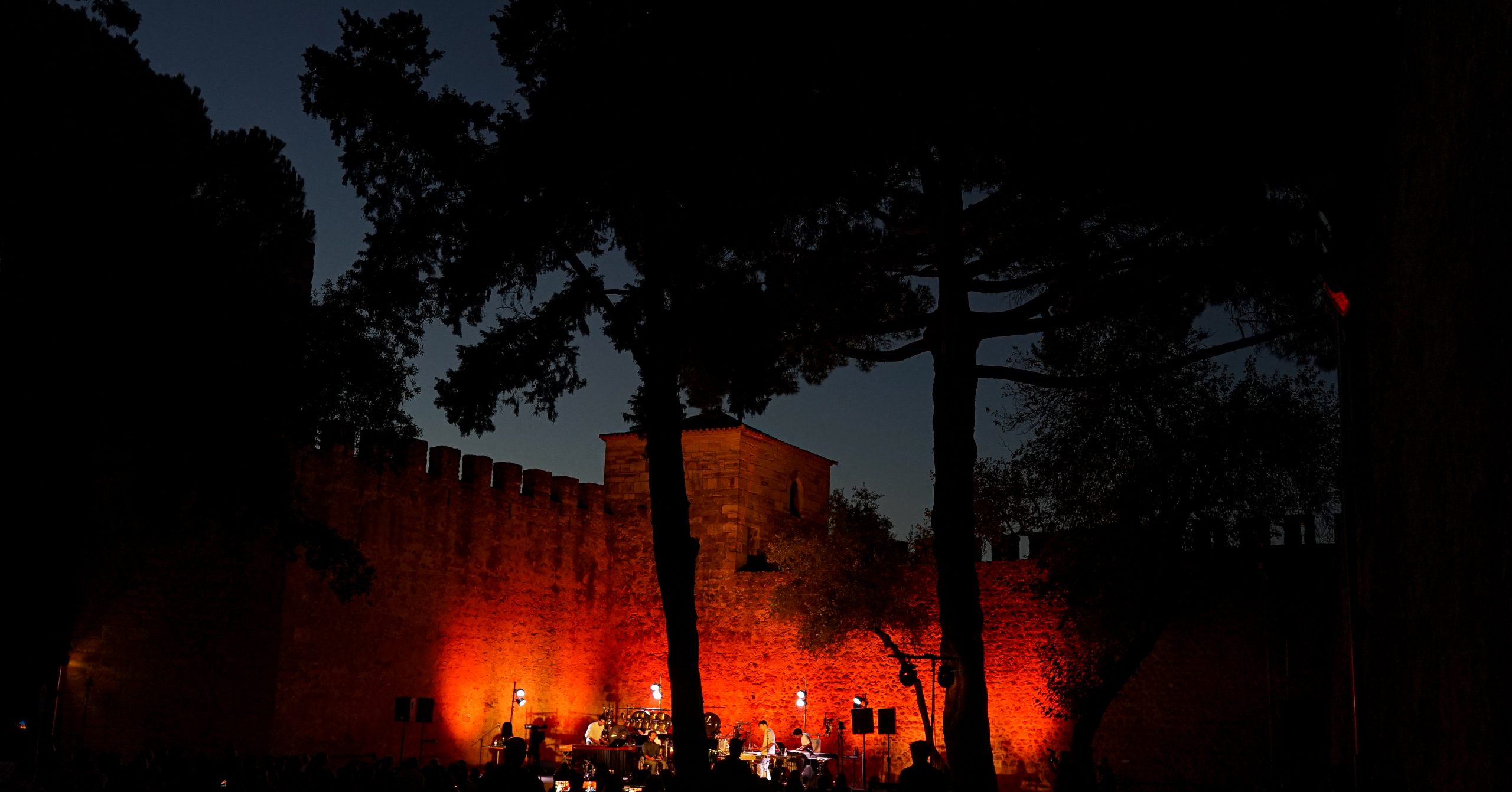 Fotografia noturna. Castelo de São Jorge, Castelejo. Palco com músicos, iluminado com luzes em tons vermelho