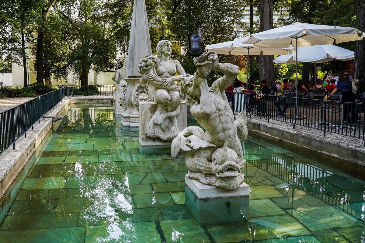 Estátuas e oblisco no lago e esplana com pessoas ao fundo.