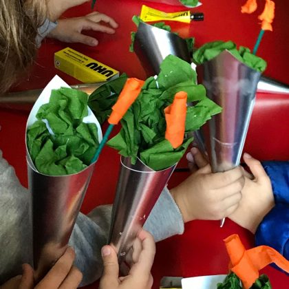 Fotografia de mãos a segurar cones de papel com folhas verdes e flores laranjas feitas em papel crepe 