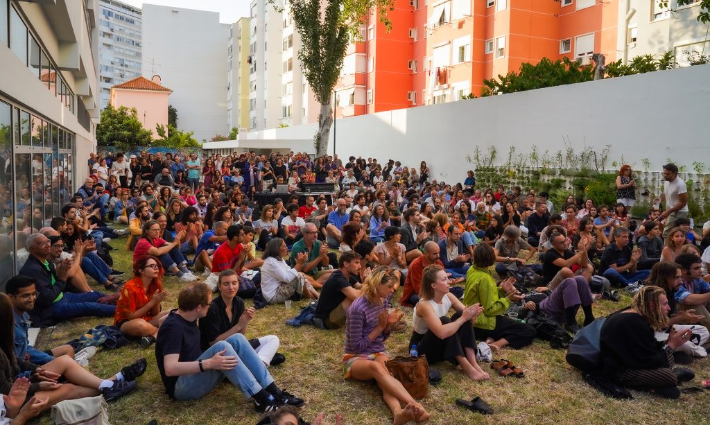 muitas pessoas sentadas na relva a assistirem a um concerto