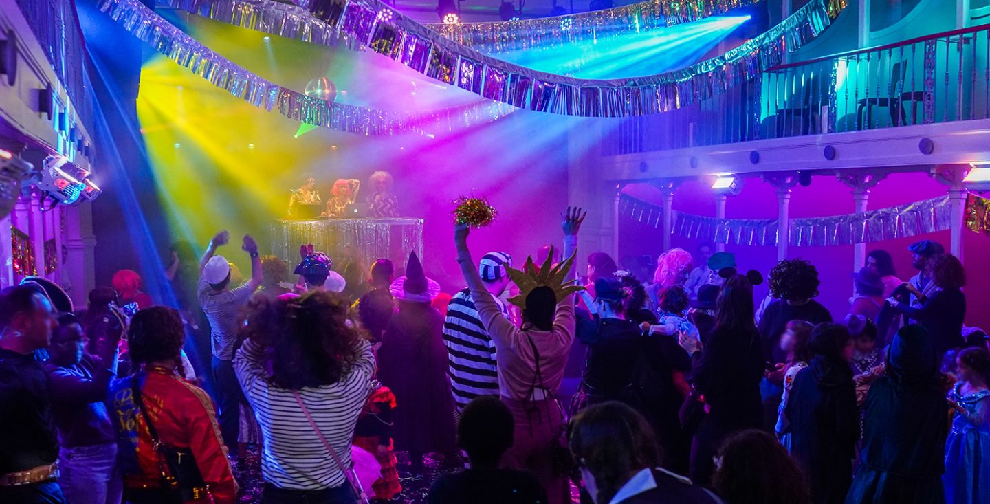 Pessoas mascaradas a dançar num espaço decorado com enfeites de carnaval