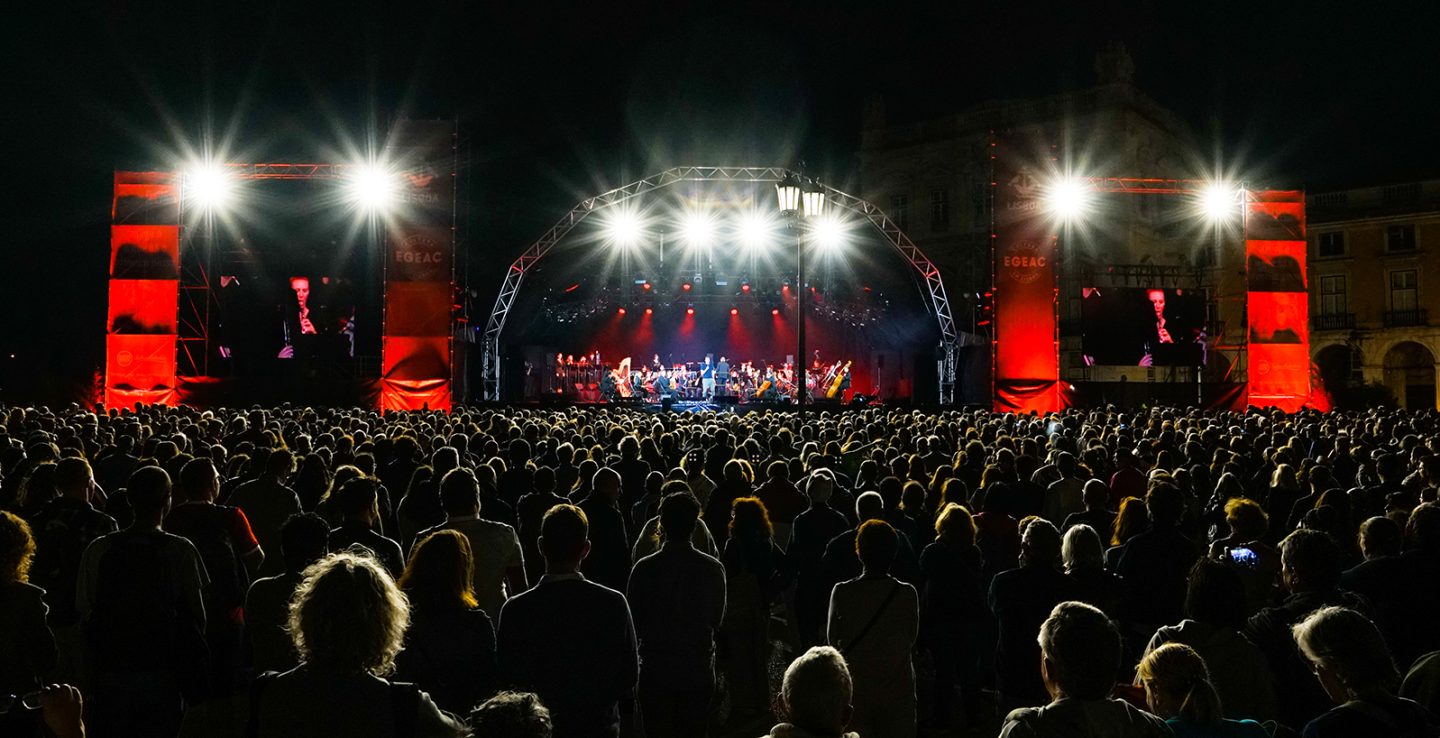 concerto à noite ao arlivre palco ao fundo e muita gente a assistir