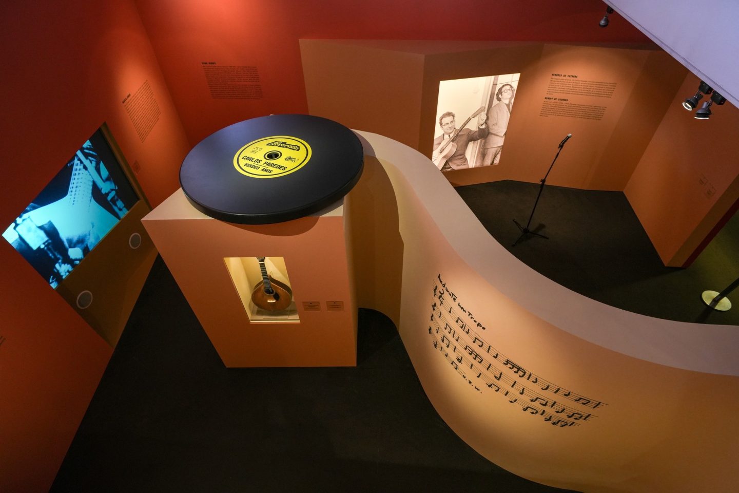 vista de cima de um sala de exposições com 1 grande disco vinil, 1 guitarra portuguesa e 1 imagem de Carlos Paredes