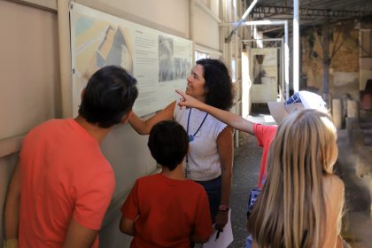 Adultos e crianças olham para um desenho pendurado numa parede no interior de um sítio arqueológico