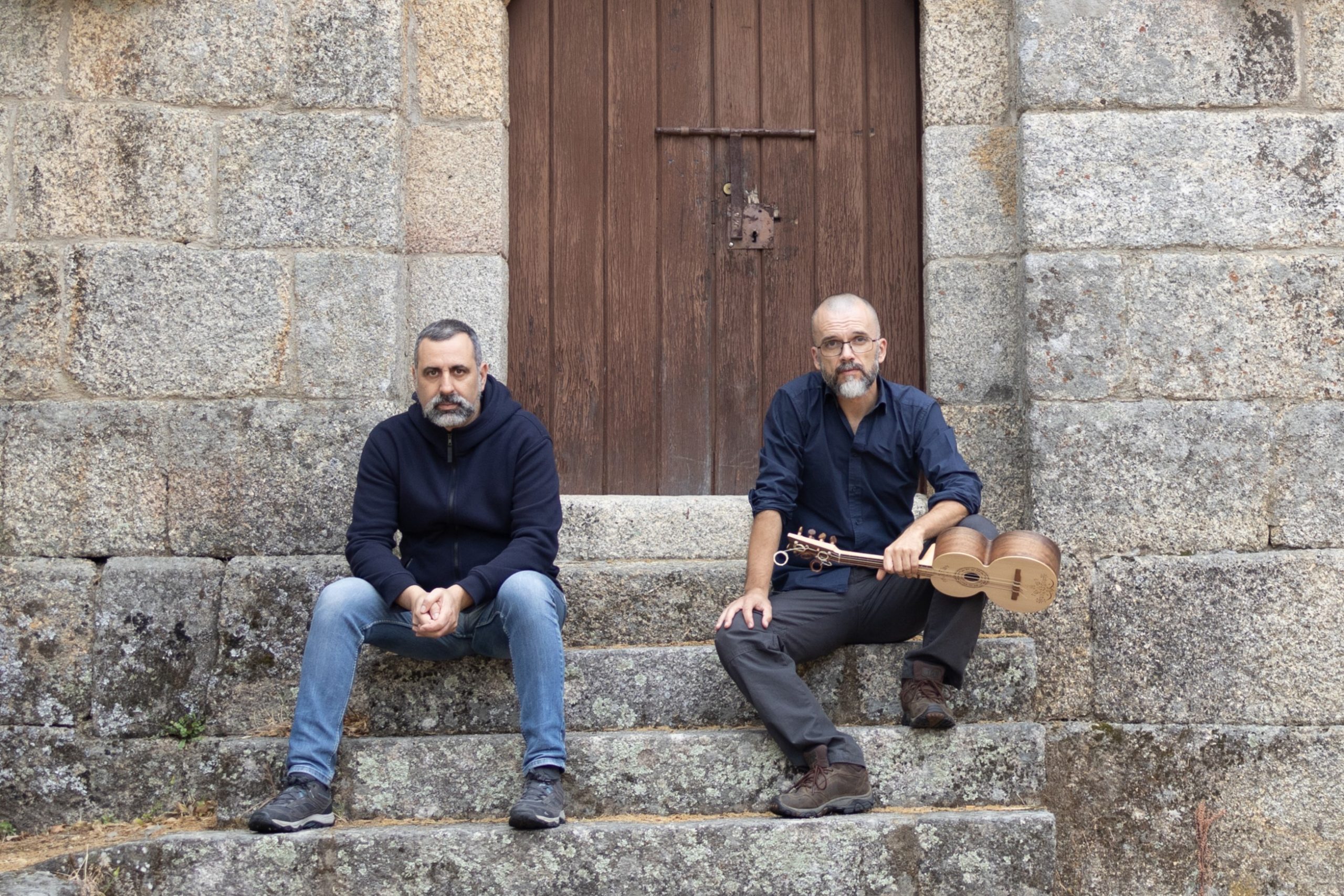 2 homens sentados nuns degraus de um edifício de pedra
