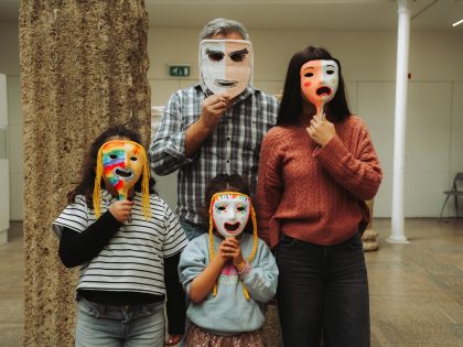 Imagem de interior, onde se vê uma coluna de pedra do lado esquerdo, com 4 pessoas, três crianças e um adulto, todos com máscaras a tapar os rostos