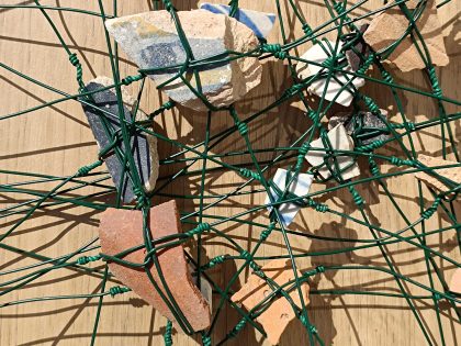 Imagem de vários fragmentos de barro embrenhados numa teia de arame verde
