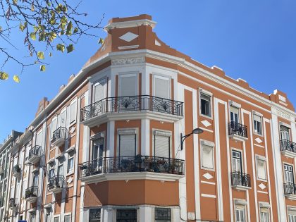 Fotografia dos dois últimos pisos de um edifício dos anos 1940, cor de tijolo e branco, com um céu azul de fundo