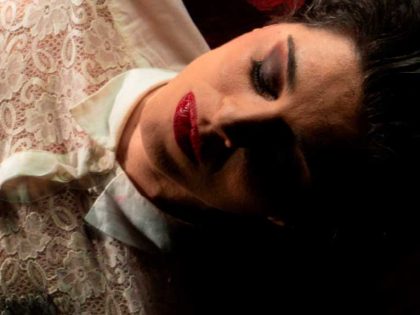 Fotografia de Catarina Molder de olhos fechados, lábios vermelhos e uma camisa de renda branca