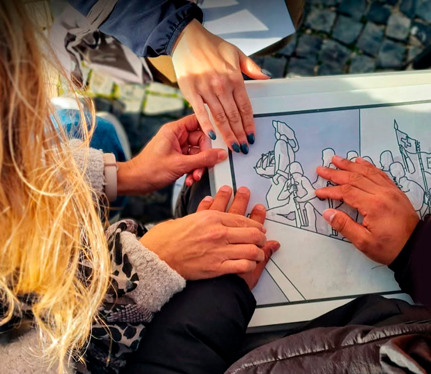 Mãos de várias pessoas exploram uma ilustração em relevo, representando uma cena com figuras humanas na proa de um barco
